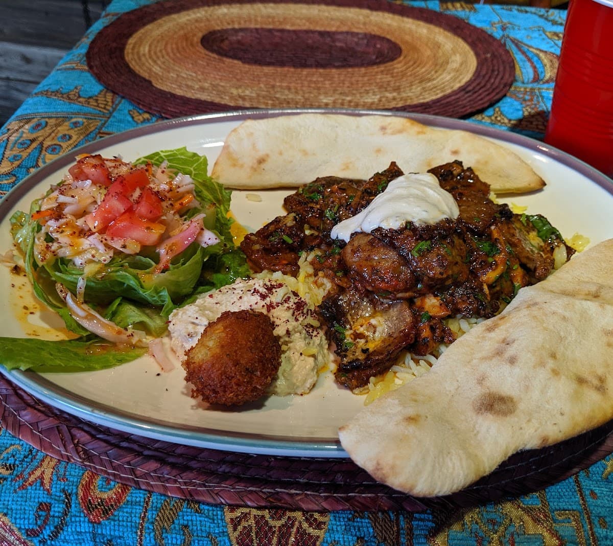 Grilled lamb platter served with hummus, salad, and folded fresh pita